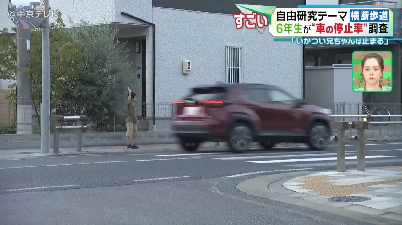 遠くの横断歩道で手を挙げる小学生の横を車が通過する