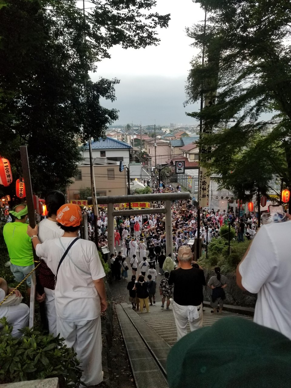 神社の石段の上から見下ろした鳥居と祭りの人だかり