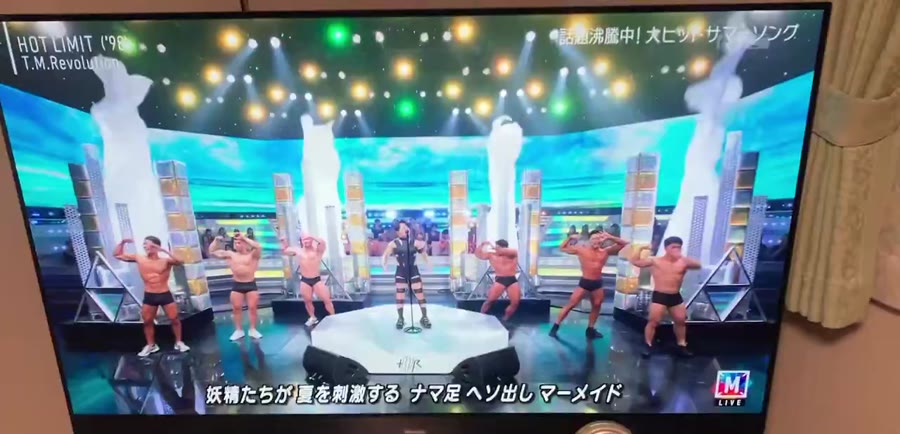 ステージ中央で歌う歌手と、両脇に並ぶボディビルダーたち