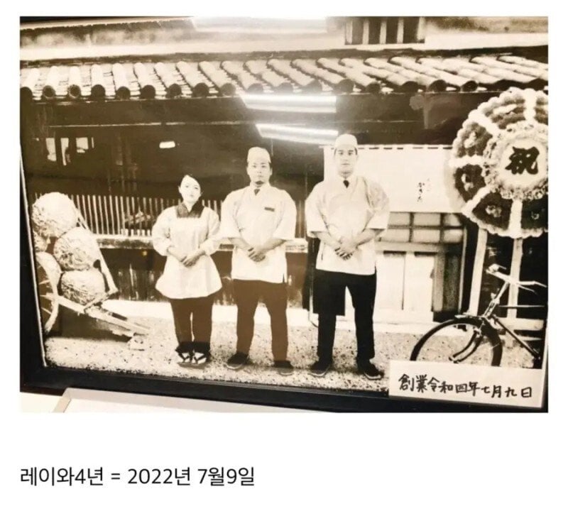 日本の店に飾られたセピア色の記念写真。右下に「創業令和四年七月九日」と書かれている